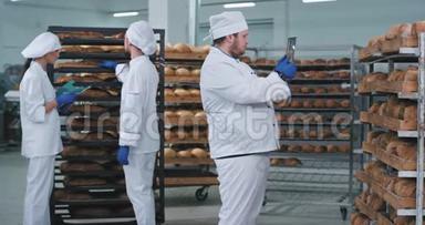 在一家面包店里，主要的面包师带着一块新的平板电脑，拍了一些新鲜烘焙面包的照片，另外两个面包师在上面。