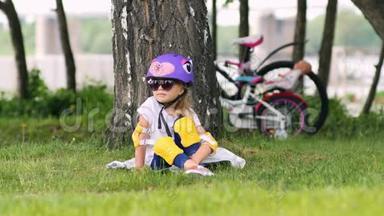 可爱的金发女孩<strong>坐在树下</strong>，戴着自行车头盔