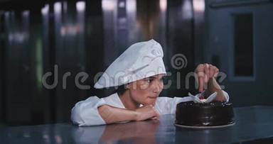 年轻漂亮的面包师小姐把樱桃从巧克力蛋糕上摘下来，高兴地笑着放进嘴里