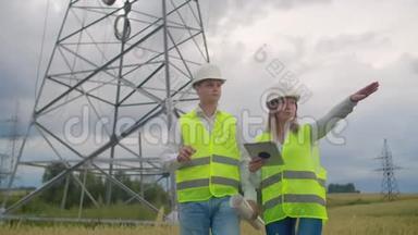 <strong>电力线</strong>路、手里拿着平板电脑的男女工程师检查新塔的安装进度