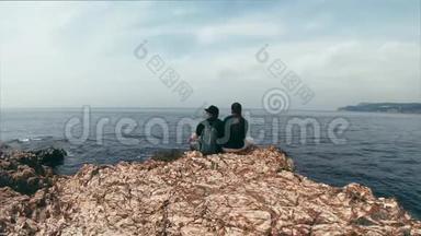 恋爱中的夫妇坐在海边的岩石边缘，谈论不同的话题，享受风景。 美丽的时光流逝