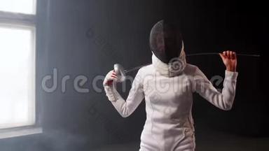一个戴着头盔的年轻女击剑运动员把剑放在工作室的肩膀后面