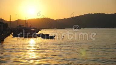 美丽的景色，渔船漂浮在海面上，背景是日落。 站在海湾的渔船