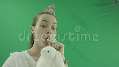 令人惊讶的兴奋的女人正在笑在生日帽与玩具和塑料口哨与全息纸管。 她穿着