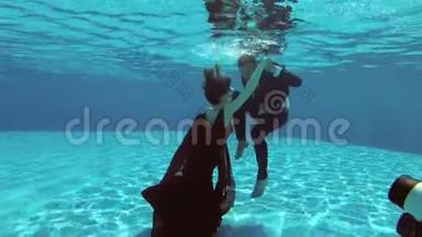 一个穿着红色裙子的漂亮女孩和一个穿西装的男人在游泳池里的水下游泳，并为一位摄影师摆姿势。