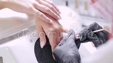 美容店里一位带手套的女美甲师用木棍把顾客指甲上的角质层推开