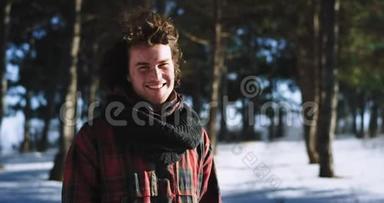 冬天的时候，有魅力的男人在镜头前的雪林中享受时光，微笑着，他带着大大的微笑