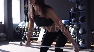 <strong>身穿</strong>黑色<strong>运动服</strong>的年轻女子在健身房内以健身为背景用杠铃做蹲姿