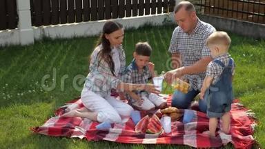 幸福的家庭坐在毯子上，父亲倒橙汁