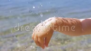 孩子们的手在<strong>水滴</strong>下，阳光反射在皮肤上。 <strong>水滴</strong>落在海边的小手上