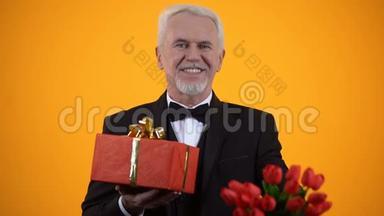 微笑的老人西装革履，献上郁金香花束和礼品盒，真诚的问候