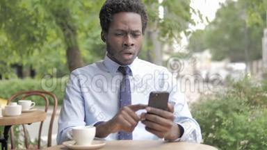 非洲商人坐在户外咖啡厅，在智能手机上失声<strong>喧哗</strong>