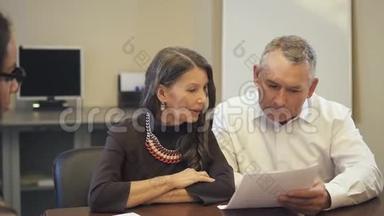 成熟夫妻在房地产中介机构阅读和讨论抵押合同。