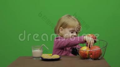 女孩坐在桌子旁吃苹果。 快乐的三岁女孩。 可爱的女孩微笑。 3-4岁金发女孩