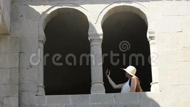 戴<strong>帽子</strong>的年轻女人自拍，坐在老窗的拱门里。 <strong>夏日</strong>阳光明媚。 旅费