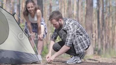 年轻人在松林里搭帐篷，而他的女朋友则站在附近。 大自然爱好者在户外放松