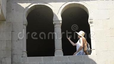 戴着背包的帽子的年轻女人自拍，坐在老窗的拱<strong>门里</strong>。 夏日阳光明媚。 旅费