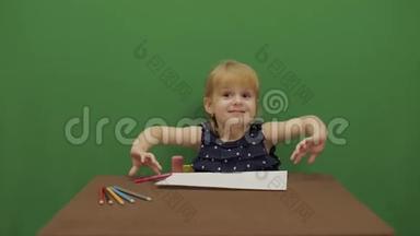 女孩在桌子边画画。 快乐的三岁女孩。 可爱的女孩微笑。 棕色的眼睛。 一个漂亮的小孩，3-4岁的女孩