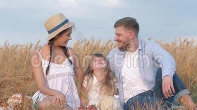 我的家庭肖像，幸福的年轻夫妇坐在他们的孩子身边，在户外微笑着看着对方