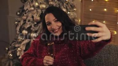 年轻迷人的女人在圣诞节的内部背景上用起泡葡萄酒制作自拍照片。 庆祝新年。