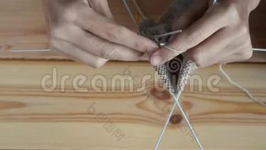 成年女孩在木桌背景上用灰色金属针和羊毛线编织