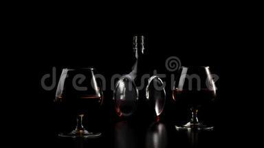 豪华白兰地。 一个圆形瓶子里的金白兰地站在黑色桌子上的两个玻璃杯旁边，背景是黑色的。 光线充足。