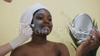 美容师用手在水疗沙龙里给年轻的非裔美国妇女敷面膜