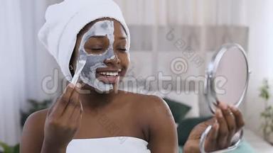 美国黑人英俊女子的肖像，头上有毛巾，<strong>半边脸</strong>上涂着黏土面具，化妆