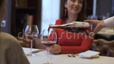 服务员在餐厅里的女孩的杯子里倒红酒，女士在微笑。 两个积极的女朋友坐在一起