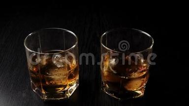 豪华威士忌。 手把冰扔到一个玻璃杯里，在黑桌上，靠近玻璃杯，有威士忌和冰。 苏格兰威士忌。