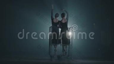 两个优雅勤奋的芭蕾舞演员在她的尖角芭蕾舞鞋上跳舞，在演播室的黑色背景上聚光灯下。 芭蕾舞