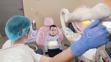 牙科医生的一个小男孩坐在病人的椅子上，牙医打开灯，张开嘴