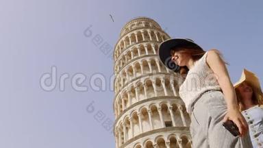 意大利比萨。 两个穿着睡衣的年轻女人走在比萨斜塔旁看着它