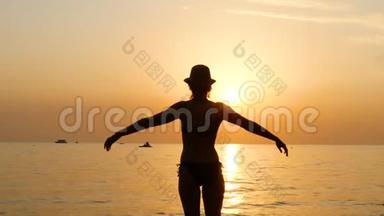 日落时分，一位戴着帽子的年轻女子站在沙滩上，穿着泳衣，举起双手