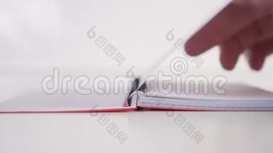 一个年轻人慢慢地翻阅一本笔记本，笔记本上有螺旋形的水平页，贴在白色的背景上