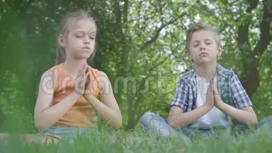 漂亮的小女孩和坐在草地上沉思的英俊男孩。 孩子们在瑜伽。 精神发展