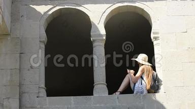 戴着背包的帽子的年轻女人自拍，坐在老窗的拱门里。 夏日阳光明媚。 旅费