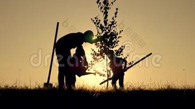 农民的幸福家庭.. 一位父亲和两个孩子在日落时在公园里<strong>种树</strong>和浇水的剪影。