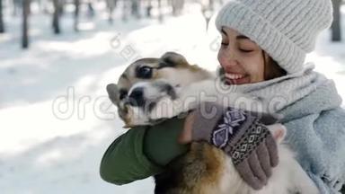 快乐的女人，戴着羊毛帽，戴着<strong>长长</strong>的温暖围巾，在寒冷的阳光明媚的日子，在下雪的冬天公园里抚摸她的宠物。 快乐