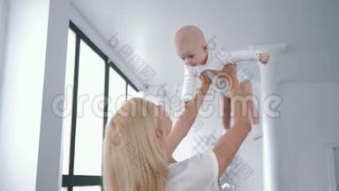 <strong>母爱</strong>，快乐的年轻妈妈把可爱的新生女儿从头上旋转，亲吻她在白色的房间里