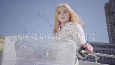 肖像可爱的金发女郎穿着温暖的白色夹克，站在<strong>城市</strong>街道上，骑着自行车<strong>看</strong>着<strong>镜头</strong>