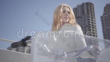 肖像美丽的金发女郎穿着温暖的白色夹克，站在<strong>城市</strong>街道上，骑着自行车<strong>看</strong>着<strong>镜头</strong>