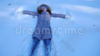 年轻的女孩躺在雪地草地上做天使。 快乐的女人在雪地里玩，享受冬天的时光。 快乐的女士