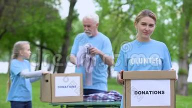 漂亮的女志愿者拿着盒子，活动家在背景上整理衣服