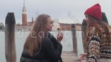 两个年轻妇女正沿着码头散步。 其中一个吃冰淇淋，然后她给她的朋友提供冰淇淋