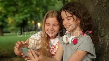 两个可爱的年轻姐妹带着耳机在美丽的日子里玩得开心。 快乐的孩子们在夏天公园玩。 看小孩
