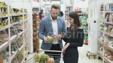 女人用智能手机检查产品清单，男人选择水果，在超市闻。
