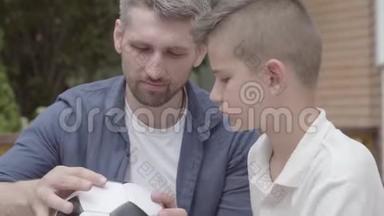 父亲和儿子坐在门廊上，手里拿着一个<strong>泄气</strong>的足球特写。 他爸爸帮孩子修