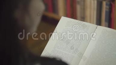 在图书馆里读一本书的年轻学生的后视图。 女孩正站在书页前面翻书
