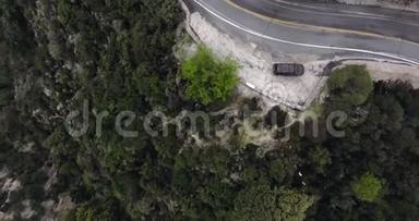 Drone在一条弯弯曲曲的路上，用一片<strong>绿油油</strong>的灌木和一辆停在路边的黑色轿车向一个长满树木的山坡射击